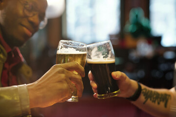 Wall Mural - Hands of two young intercultural men clinking with glasses of beer in the pub