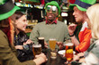 Group of young intercultural friends in traditional irish attire having beer
