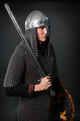 Portrait of a medieval warrior of the late Viking era and the beginning of the Crusades. Knight in chain mail and helmet armed with a shield and sword isolated on a dark background.