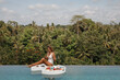© Yevhenii - Attractive young girl having breakfast in swimming pool with tropical jungle view, eat croissant and drink coffee