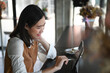 © Prathankarnpap - Happy young woman freelancer sitting at wooden bar in coffee shop and working on computer tablet.