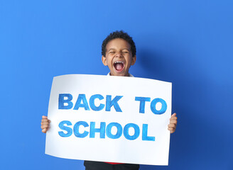 Wall Mural - Happy little African-American boy holding placard with text BACK TO SCHOOL on color background