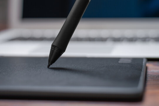 Image of a graphics tablet, stylus and laptop on a wooden table. Designer workplace. Freelance. Retouching. IT concept.