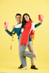 Sticker - Happy beautiful young Asian couple in winter clothes showing lucky money envelops and garlands of sycee or Chinese gold ingots