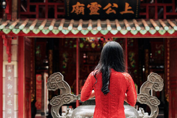 Sticker - Young woman in red dress praying at urn with incense sticks at Buddhist temple on Spring festival, view from the back