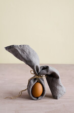 Creative Easter Bunny, Natural Unpainted Chicken Egg Is Wrapped In A Gray Napkin And Stands On A Beige Background. Minimalism, Brown Monochrome, Vertical Background