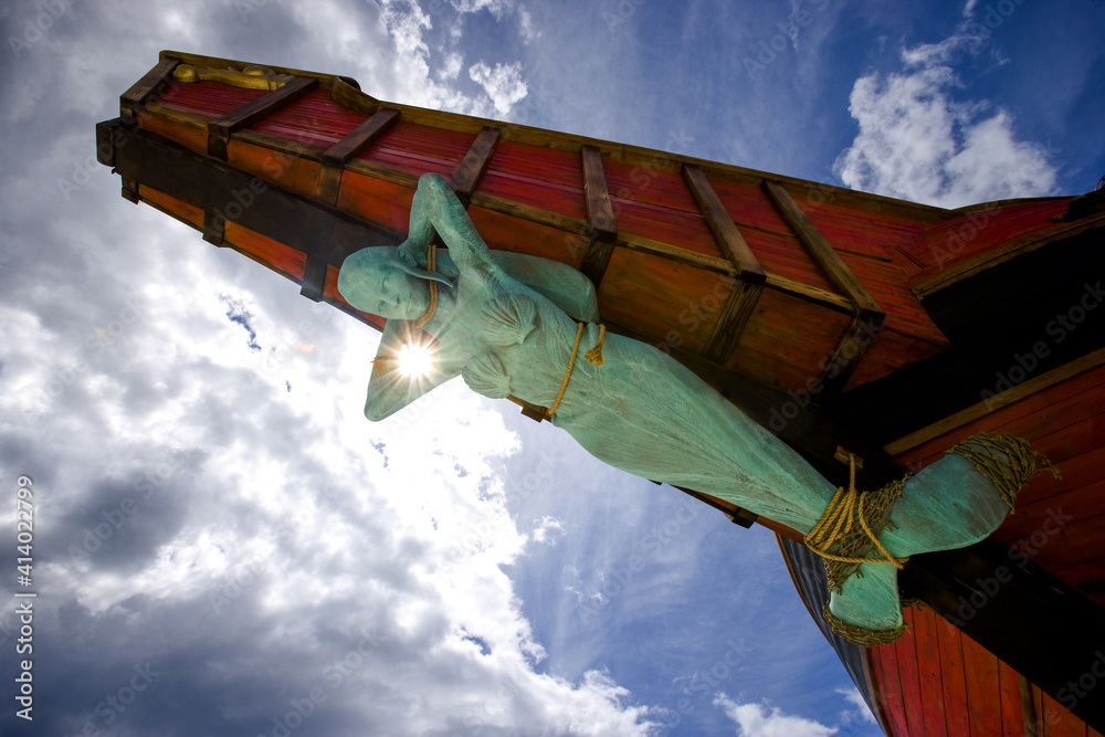 A Statue of a Mermaid Tied Up to the Bow of a Ship with Blue Sky and Clouds in the Background - obrazy, fototapety, plakaty 