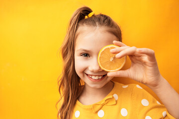 Happy cute girl with clean perfect skin hiding eye behind lemon slice on yellow background