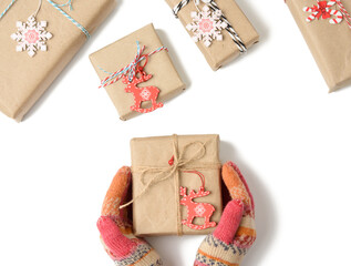 Wall Mural - female hands in knitted mittens hold a box wrapped in brown paper and tied with a rope on a white background