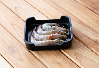 Wall Mural - fresh raw shrimp sliced on square plate isolated on wooden background, shabu, hot pot ingredients