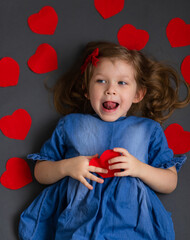 Top view of a happy little girl in a blue dress. The girl holds a red paper heart in front of her. The concept of Valentine's Day and 8 March.