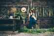 Attractive girl wearing straw hat and blue denim dungarees relaxing near wooden old summerhouse wall on sunny day.