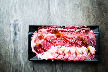 fresh raw pork, meat ,beef, belly, sliced on square plate  on fabric and wood, wooden background, shabu, hot pot ingredients.