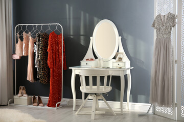 Wall Mural - Rack with collection of beautiful festive clothes and dressing table in stylish room interior