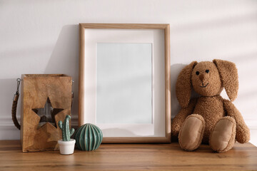 Poster - Empty photo frame near cute toy bunny and decor on wooden table, space for text. Baby room interior element