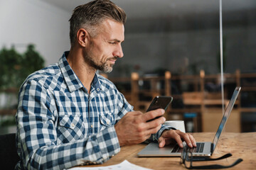 Wall Mural - Focused grey man using mobile phone while working with laptop