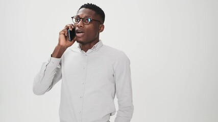 Poster - A serious african american man wearing glasses is talking on his smartphone standing isolated over white background in studio