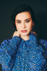 Fashion portrait of stylish young brunette woman wearing blue animal pring clothes, posing on black background