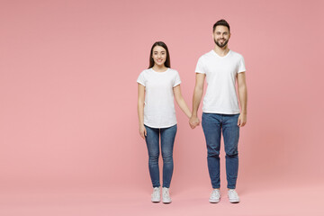 Wall Mural - Full body length young cheerful couple two friends bearded man brunette woman in white basic blank print design t-shirts jeans standing posing isolated on pastel pink color background studio portrait.