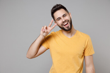 Wall Mural - Young caucasian smiling happy bearded satisfied attractive man 20s wear casual yellow basic t-shirt showing victory v-sign gesture isolated on grey background studio portrait People lifestyle concept.