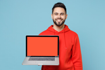 Wall Mural - Young caucasian smiling satisfied copywriter freelancer bearded man 20s in casual red orange hoodie hold laptop pc computer, blank screen workspace area isolated on blue background studio portrait