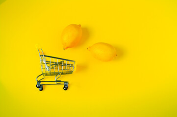 Lemon in shopping cart, shopping trolley on yellow background. Shopping concept. Basket of fresh lemons isolated on yellow background. Vitamin C.