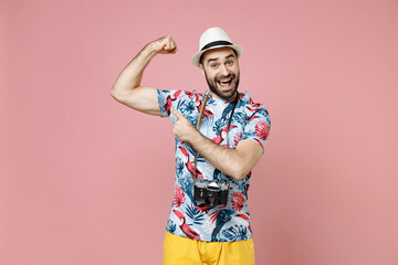 Wall Mural - Excited young traveler tourist man in summer clothes hat with photo camera point index finger on biceps muscles isolated on pink background. Passenger traveling on weekend. Air flight journey concept.