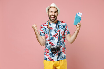 Canvas Print - Happy young traveler tourist man in summer clothes hat hold passport ticket boarding pass doing winner gesture isolated on pink background. Passenger traveling on weekends. Air flight journey concept.