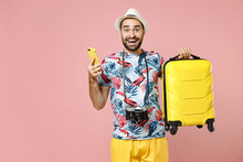 Excited Young Traveler Tourist Man In Summer Clothes Hat Hold Suitcase Using Mobile Phone Booking Taxi Hotel Isolated On Pink Background. Passenger Traveling On Weekends. Air Flight Journey Concept.
