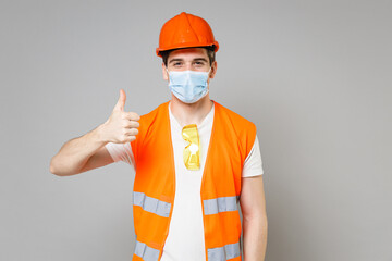 Poster - Young employee man in orange vest protective helmet face mask, coronavirus covid-19 show thumb up gesture isolated on grey background studio Instruments for renovation apartment Repair home concept