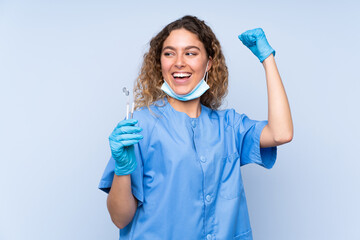 Wall Mural - Young blonde woman dentist holding tools isolated on blue background celebrating a victory