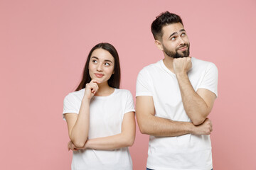 Wall Mural - Young pensive couple two friends bearded man brunette woman in white basic blank print design t-shirts thinking dream put hand prop up on chin isolated on pastel pink color background studio portrait.