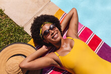 Mixed race woman sunbathing by pool on a sunny day smiling