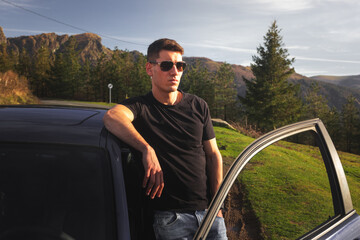 Young caucasian man posing outside of a sports car on the mountain