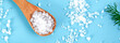 Coarse salt crystals on a blue table. Wooden spoon with sea salt. Background for advertising salty. Banner
