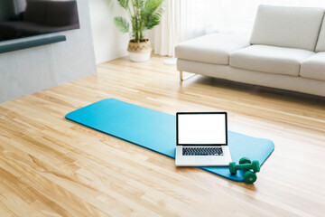 Online workout at home gym concept. Laptop computer on yoga mat on floor in living room in modern apartment interior