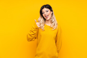 Wall Mural - Teenager girl isolated on yellow background showing ok sign and thumb up gesture