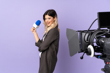 Reporter teenager girl holding a microphone and reporting news isolated on purple background with arms crossed and looking forward