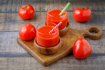 Tomato juice in glasses with straws on wooden boards