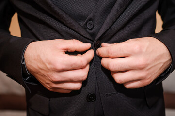 The groom buttons his jacket