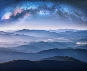 Wall Mural - milky way arch over the mountains in fog at starry night in summer. landscape with blue sky with sta