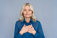 Happy Mindful Thankful Middle Aged Old Woman Holding Hands On Chest Meditating With Eyes Closed Isolated On Grey Background Feeling No Stress, Gratitude, Mental Health Balance, Peace Of Mind Concept.