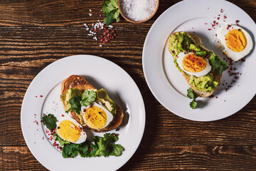 Poached egg and avocado  on sliced toasted bread, two plates, top view