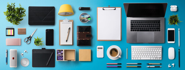 Flat lay top view office desk working space with laptop and supplies on blue background.