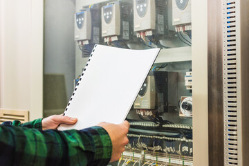 Man wearing a green checkered shirt doing the maintenance of electronic meters holding a checking notebook