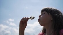 Cute Girl Blowing Dandelions On A Background Of Blue Sky. Slow Motion