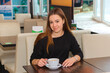 © Ksenia Belyaeva - young beautiful woman drinking coffee at a table in a cafe