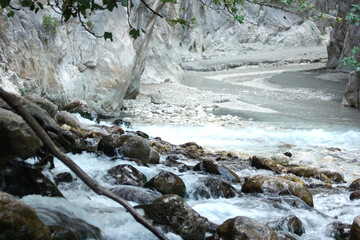 Landscape of mountain river with stones. Water streaming through rocks in a creek. Sandstone formations in the background.