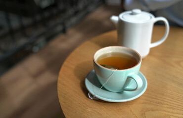 A cup of hot tea with tea pot on a wood table in a cafe