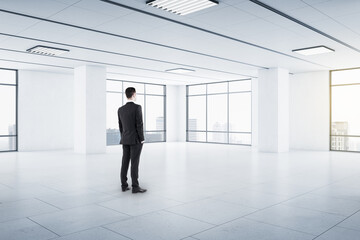 Canvas Print - Businessman in black suit in empty spacious hall room with light walls, big windows